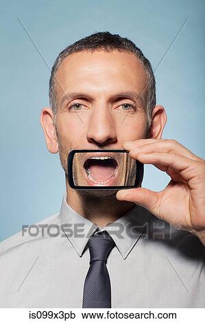 Stock Image - Man with smartphone over mouth. Fotosearch