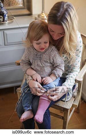 Stock Image - Mother helping daughter put on socks. Fotosearch