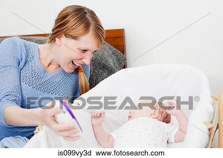 Stock Image - Mother smiling at newborn daughter in bassinet. Fotosearch