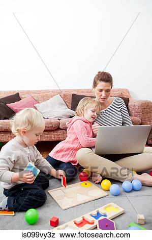 Stock Photo - Mother using laptop, children playing. Fotosearch