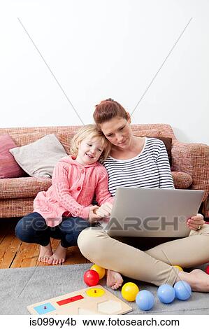 Stock Image - Mother using laptop with daughter. Fotosearch
