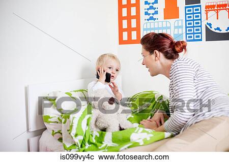 Stock Image - Mother with son in bed on cell phone. Fotosearch