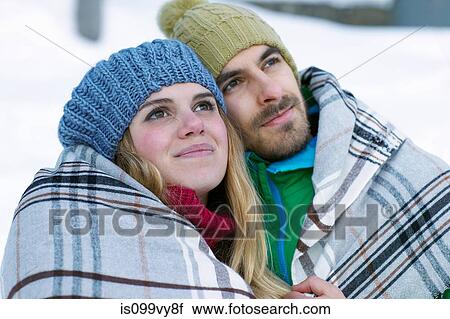 Stock Image - Portrait of couple wearing knit hats, wrapped in blanket. Fotosearch