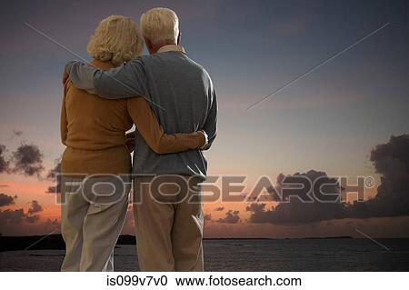 Stock Image - Senior couple looking out to sea together at sunset. Fotosearch