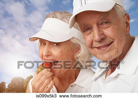 Stock Image - Senior tennis couple eating strawberries. Fotosearch