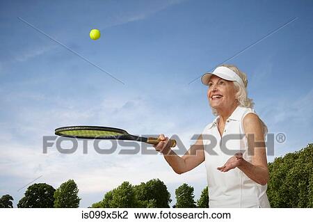 Stock Image - Senior woman bouncing tennis ball on rocket. Fotosearch