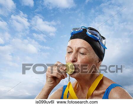 Senior woman wearing swimming cap kissing gold medal View Large Photo Image Stock Image - Senior woman wearing swimming cap kissing gold medal. Fotosearch