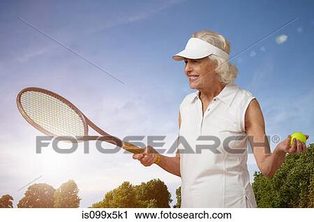 Stock Image - Senior woman with tennis racket and ball. Fotosearch