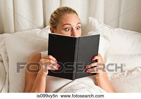 Picture - Surprised woman reading book in bed. Fotosearch
