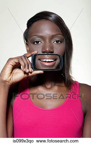 Picture - Teenage girl holding smartphone over mouth. Fotosearch
