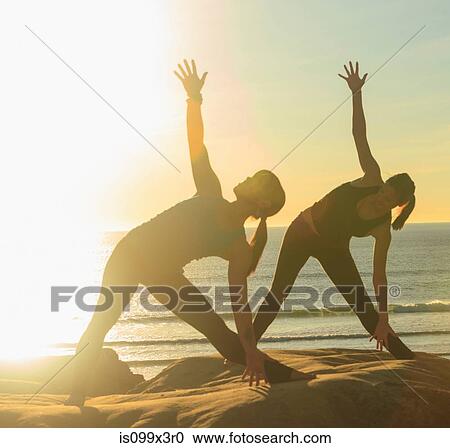 Two women practising yoga on beach in sunlight View Large Photo Image Stock Image - Two women practising yoga on beach in sunlight. Fotosearch