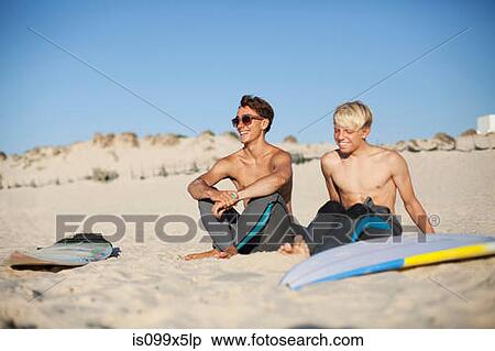 Stock Photography - Two young surfers sitting on a beach. Fotosearch