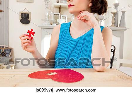 Stock Image - Woman doing heart shaped jigsaw puzzle holding piece. Fotosearch