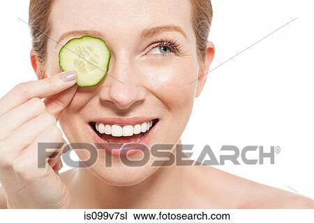 Stock Image - Woman holding a cucumber slice to her eye. Fotosearch
