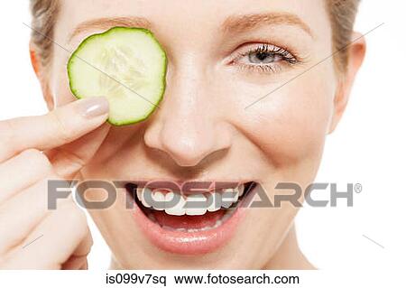 Woman holding a cucumber slice to her eye View Large Photo Image Stock Photography - Woman holding a cucumber slice to her eye. Fotosearch