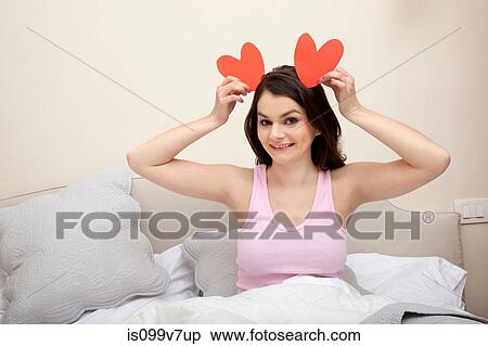 Stock Photography - Woman in bed holding heart shapes as ears. Fotosearch