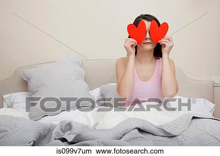 Woman in bed holding heart shapes over eyes View Large Photo Image Picture - Woman in bed holding heart shapes over eyes. Fotosearch