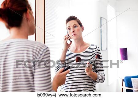 Stock Image - Woman on cell phone applying make up. Fotosearch