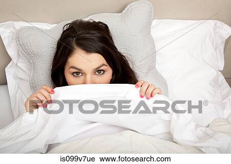 Stock Image - Woman peeking behind duvet. Fotosearch