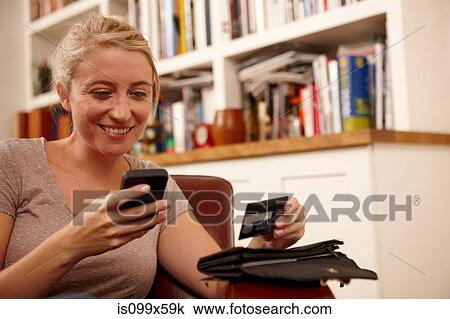 Stock Image - Woman using smartphone, holding credit card. Fotosearch
