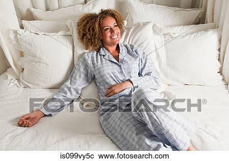 Stock Image - Woman wearing pyjamas reclining in bed. Fotosearch
