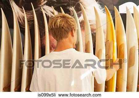 Young man looking at surfboards View Large Photo Image Stock Image - Young man looking at surfboards. Fotosearch