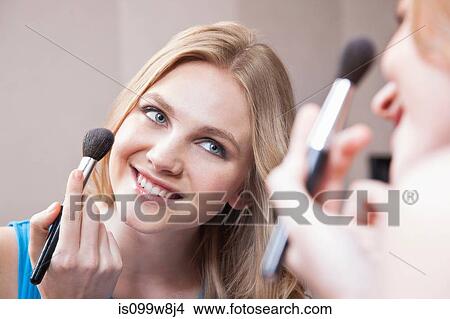 Young woman applying blusher in the mirror View Large Photo Image Picture - Young woman applying blusher in the mirror. Fotosearch