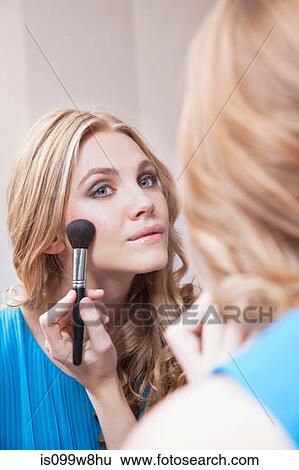 Stock Photograph - Young woman applying blusher in the mirror. Fotosearch