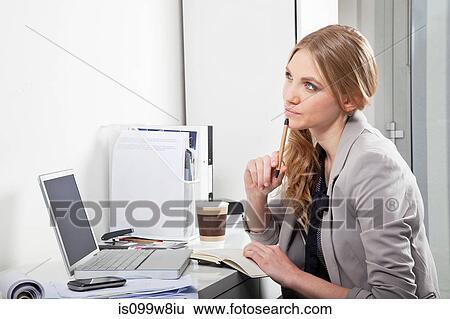 Stock Photograph - Young woman at her desk, thinking. Fotosearch