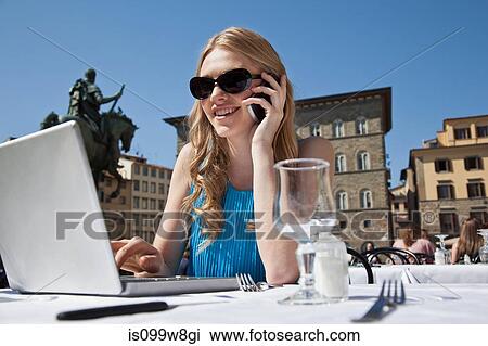 Young woman at restaurant outdoors, using laptop and cellphone View Large Photo Image Stock Image - Young woman at restaurant outdoors, using laptop and cellphone. Fotosearch