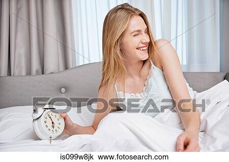 Young woman in bed, holding an alarm clock View Large Photo Image Stock Image - Young woman in bed, holding an alarm clock. Fotosearch