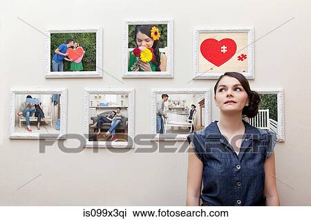 Stock Image - Young woman in front of wall of photographs. Fotosearch