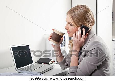 Stock Image - Young woman in office with cellphone and coffee. Fotosearch
