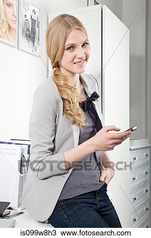 Stock Image - Young woman in office with cellphone. Fotosearch