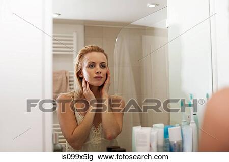 Stock Image - Young woman looking in bathroom mirror. Fotosearch