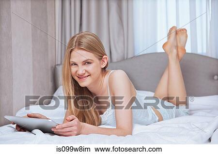 Picture - Young woman lying on bed and using digital tablet. Fotosearch