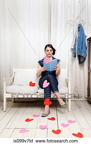 Stock Image - Young woman reading book with heart shapes. Fotosearch