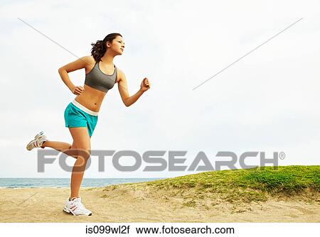 Stock Image - Young woman running on beach. Fotosearch