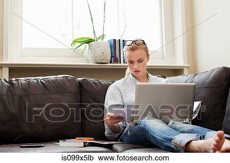 Young woman sitting on sofa with laptop and papers View Large Photo Image Stock Image - Young woman sitting on sofa with laptop and papers. Fotosearch