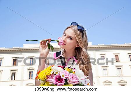 Stock Image - Young woman smelling rose from bouquet of flowers. Fotosearch