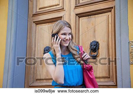 Stock Photo - Young woman using cellphone near doors. Fotosearch