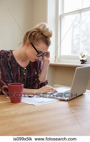 Stock Image - Young woman wearing glasses, using laptop. Fotosearch