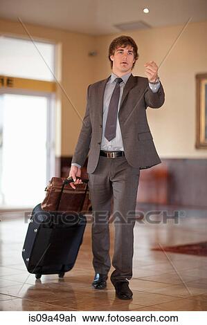 Businessman rolling luggage in lobby View Large Photo Image Stock Image - Businessman rolling luggage in lobby. Fotosearch