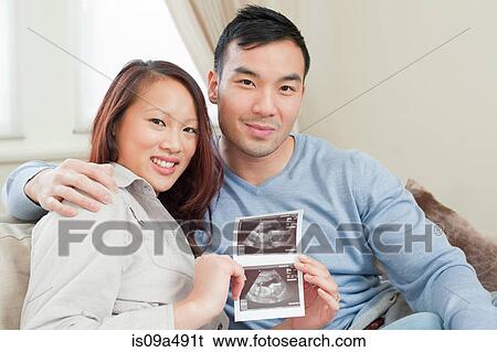 Couple displaying sonogram on sofa View Large Photo Image Stock Photograph - Couple displaying sonogram on sofa. Fotosearch