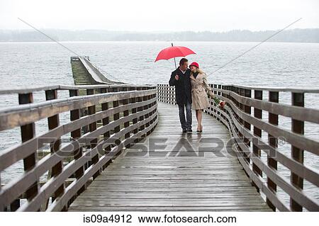 Stock Image - Couple walking on wooden pier in rain. Fotosearch
