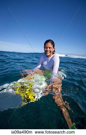 Picture - Girl sitting on surfboard in water. Fotosearch