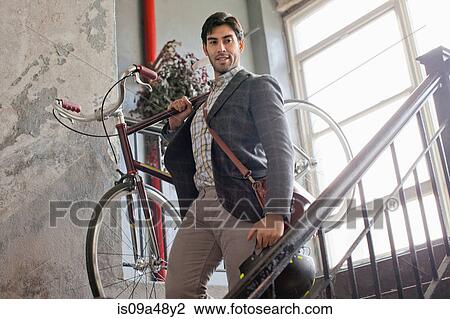Stock Image - Man carrying bicycle down staircase. Fotosearch