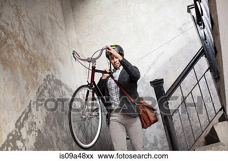 Stock Photo - Man carrying bicycle down staircase. Fotosearch