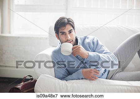 Stock Photo - Man drinking cup of coffee on sofa. Fotosearch