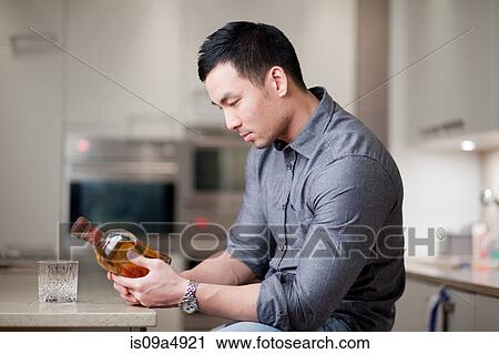 Man examining whiskey bottle in kitchen View Large Photo Image Stock Image - Man examining whiskey bottle in kitchen. Fotosearch